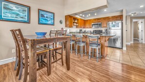 A modern kitchen with wooden cabinets, a central island with bar stools, and a dining area with a wooden table and chairs.