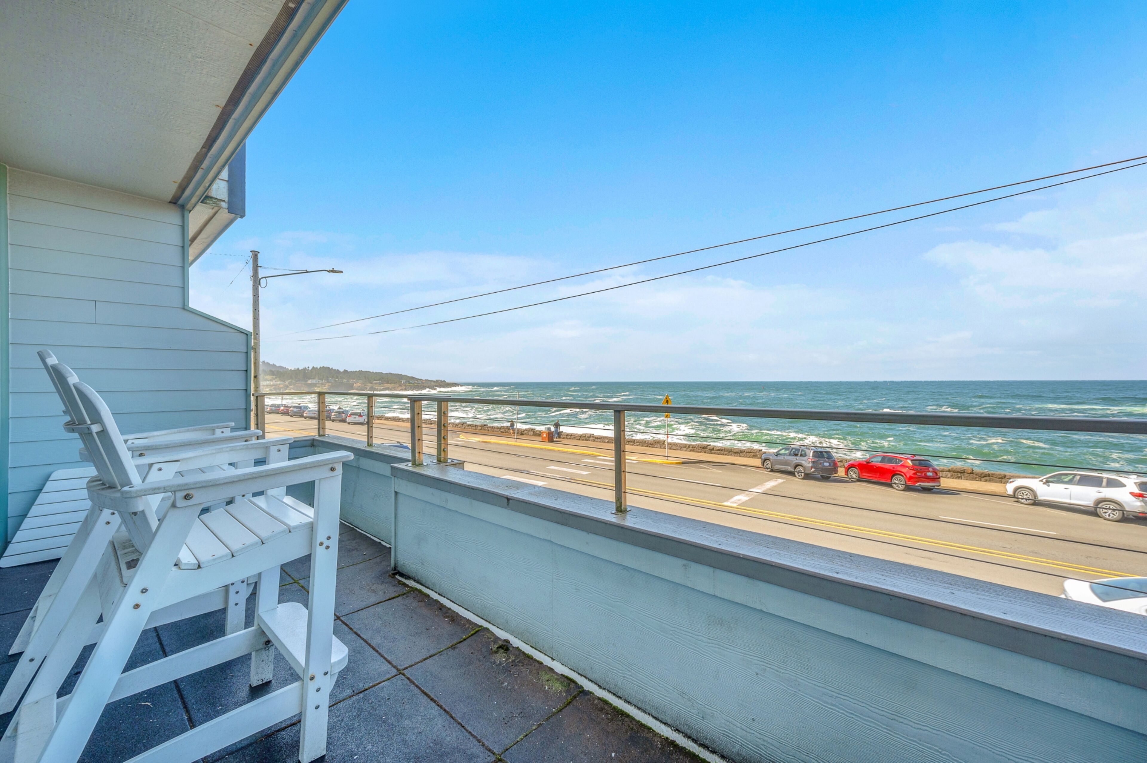 A balcony with a view of the ocean and a road with cars.