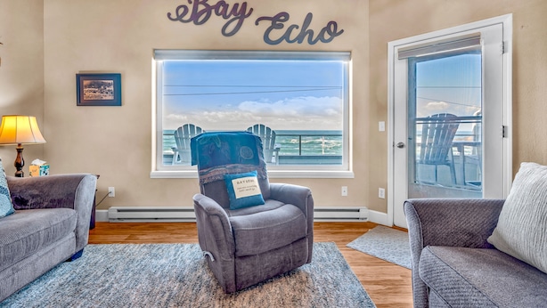A living room with a gray armchair, a couch, a large window with a view, and a wall sign reading 'Bay Echo'.