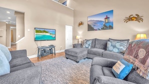 A living room with a grey sofa set, a flat-screen TV, a lamp, and a painting of a lighthouse.