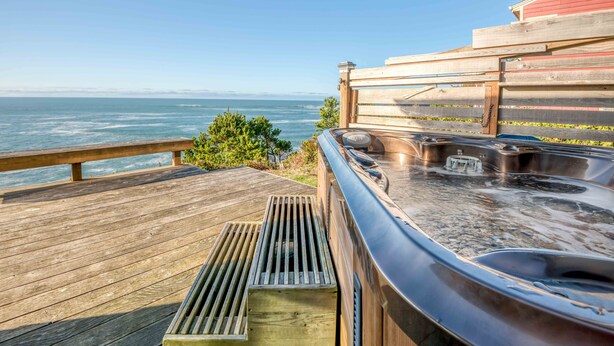 Une terrasse en bois avec un jacuzzi et vue sur l’océan.