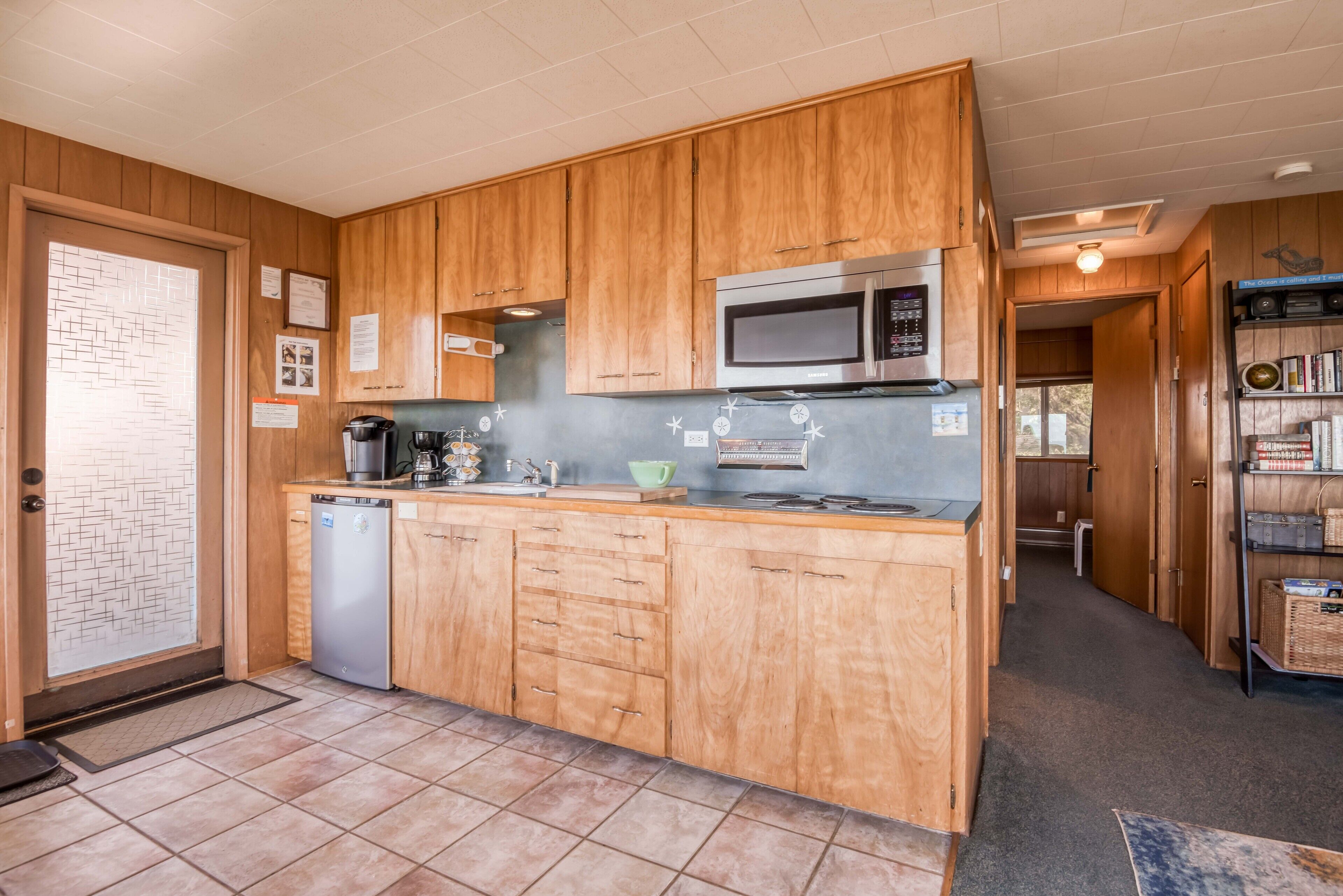 A compact kitchen with wooden cabinets, a microwave, a coffee maker, and a dishwasher.