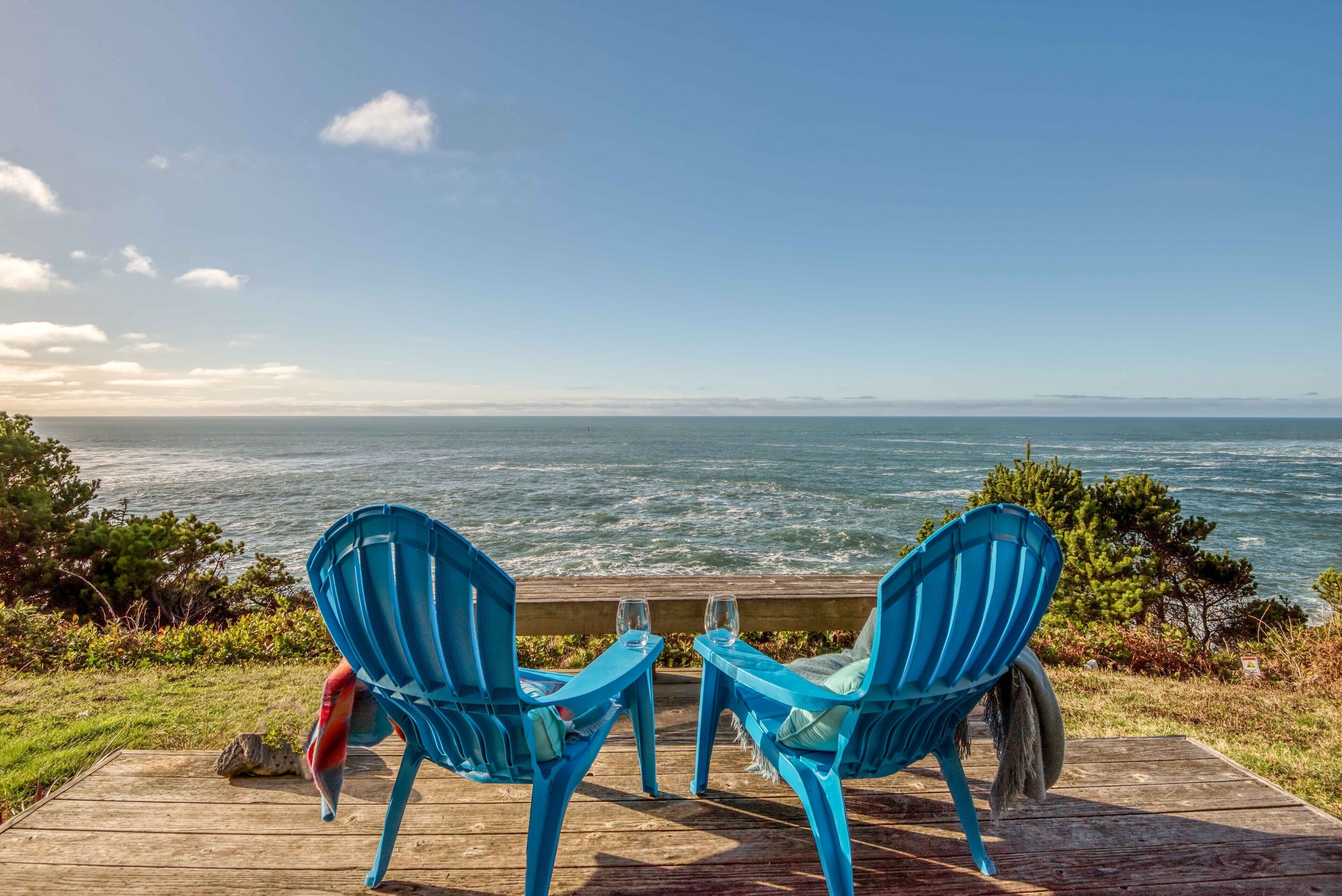 Zwei blaue Stühle auf einer Holzterrasse mit Blick auf das Meer.