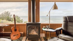 Une pièce chaleureuse avec un poêle à bois, une guitare et une vue sur l’océan.