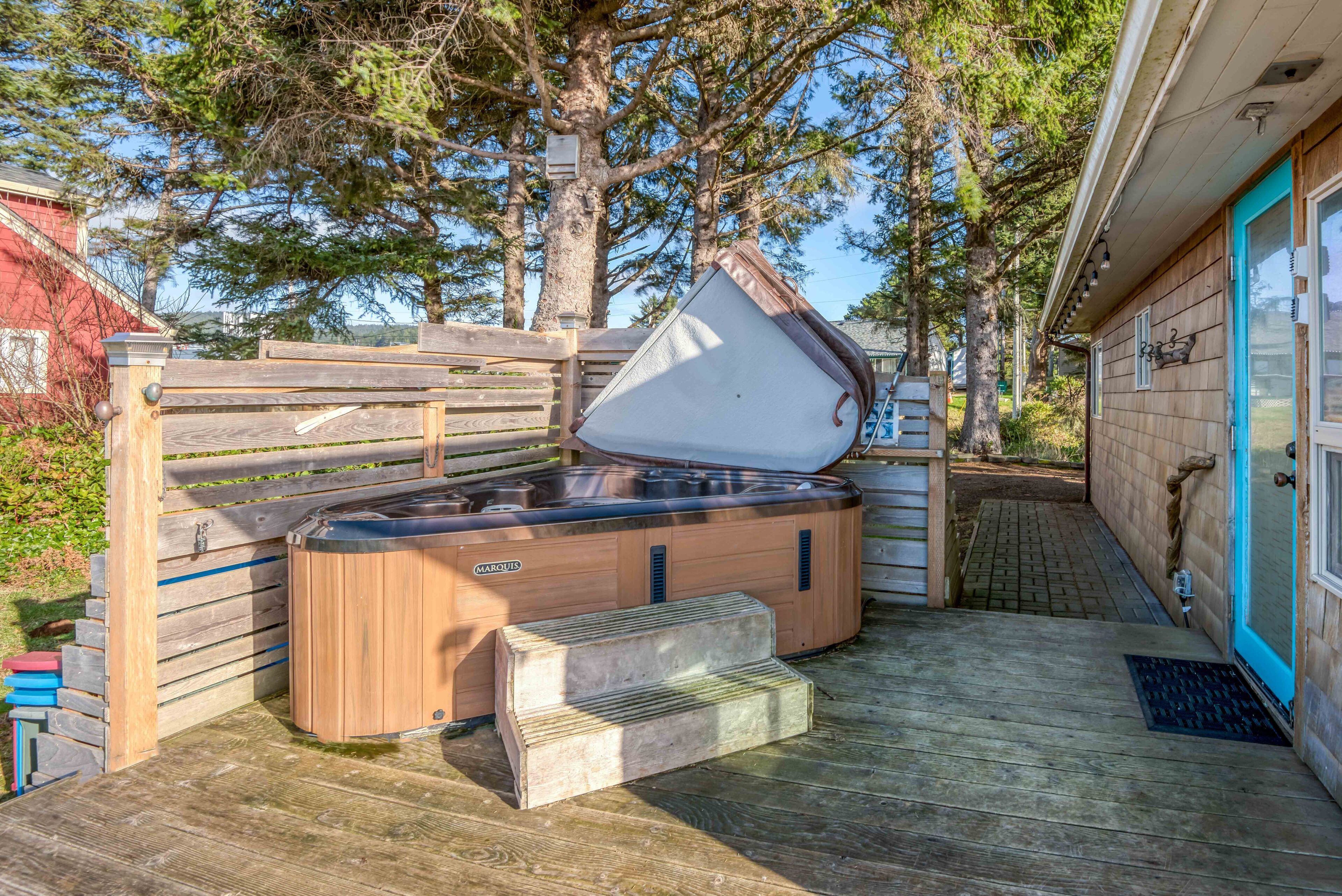 Un bain à remous avec une terrasse en bois, une clôture en bois et une maison en arrière-plan.