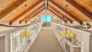 A high-ceilinged attic room with a rope railing, a view through a sliding door, and a carpeted floor. - Beautiful home with ocean views, easy beach access and wheelchair accessible (Lincoln City)