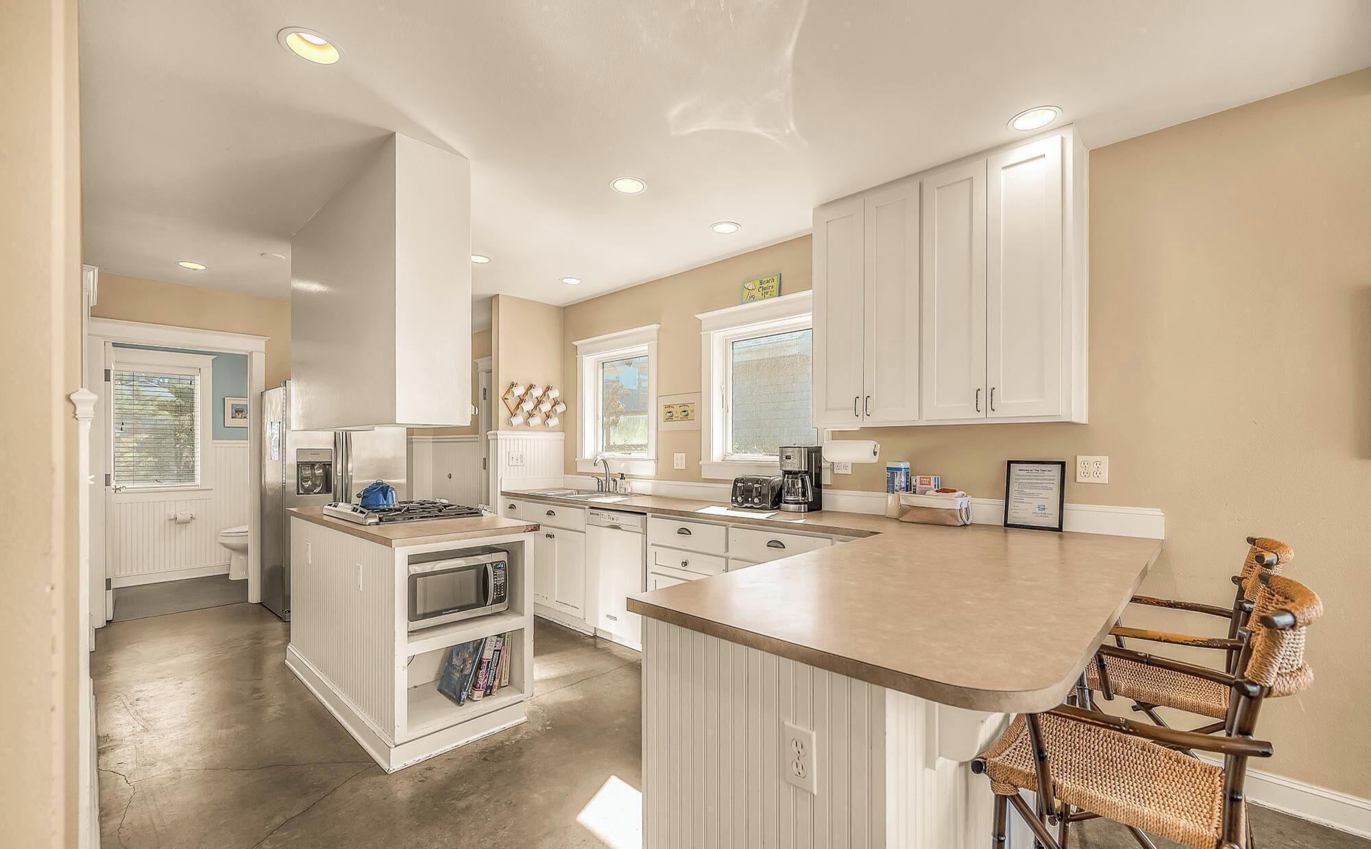 A modern kitchen with white cabinetry, a central island with bar stools, and a view of the backyard through the window.