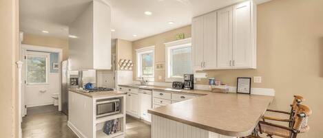 A modern kitchen with white cabinetry, a central island with bar stools, and a view of the backyard through the window.