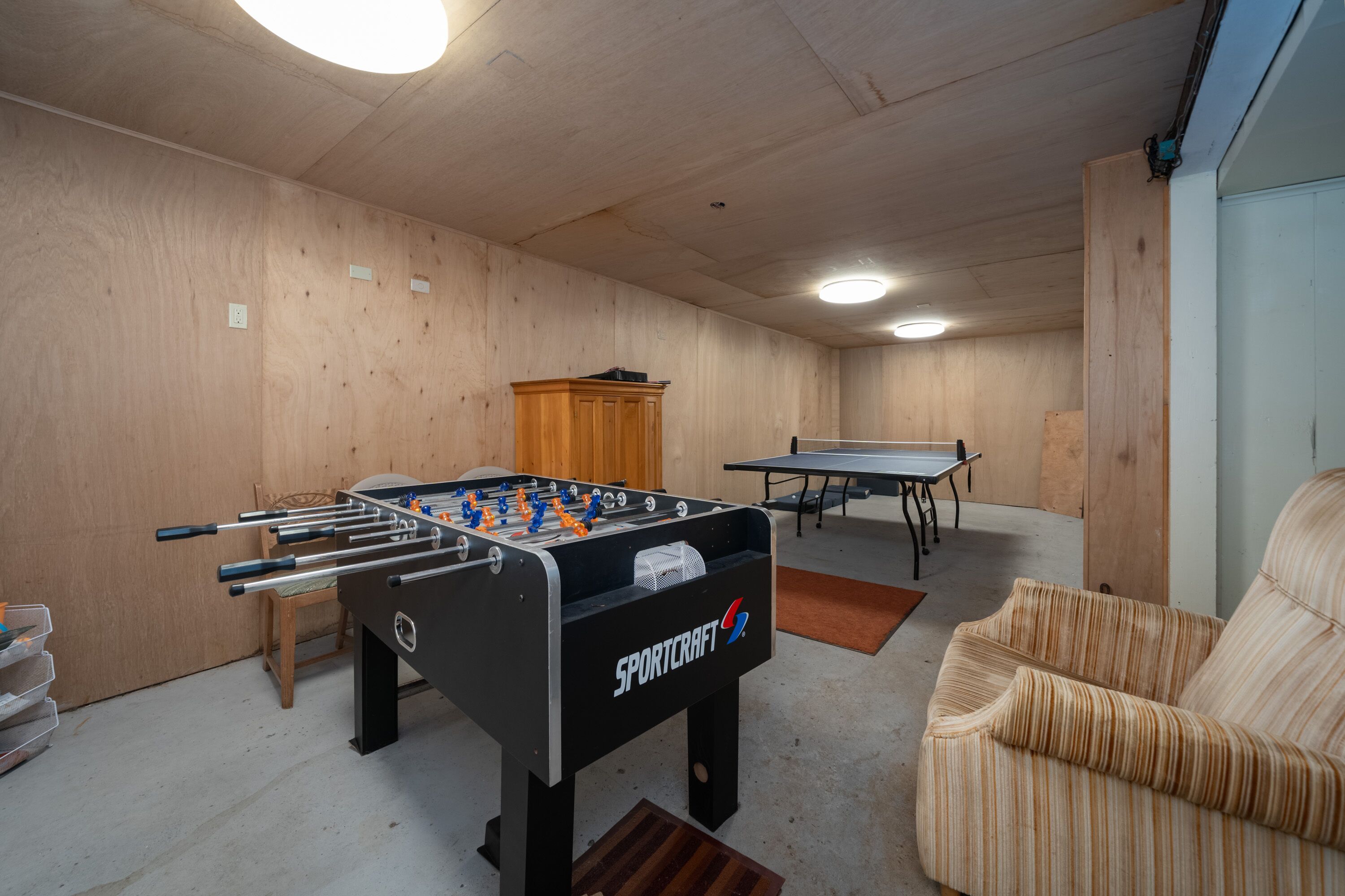 A room with a foosball table, ping pong table, and a wooden cabinet.