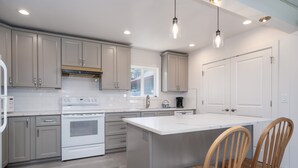 Una cocina moderna con armarios grises, una isla blanca, sillas de madera e iluminación colgante.