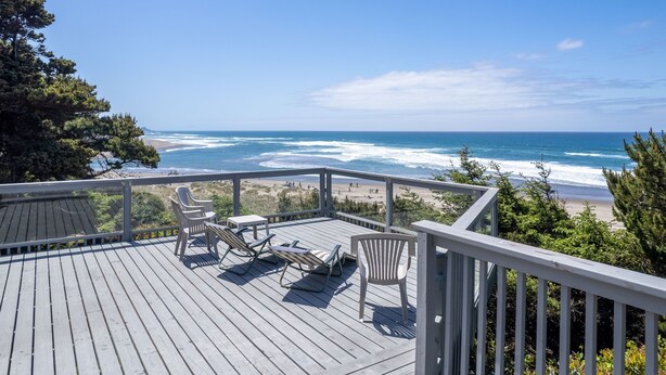 Una terraza de madera con mobiliario exterior con vista a una playa y el océano.