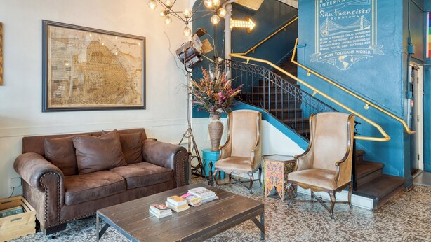 A lobby with a brown leather sofa, a wooden coffee table with books, a blue staircase, and a wall with a map and text. - HI San Francisco Downtown Hostel (San Francisco)