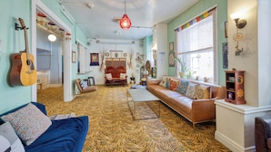 A cozy living room with a patterned carpet, a blue sofa, a brown leather couch, and a guitar leaning against the wall. - HI San Francisco Downtown Hostel (San Francisco)
