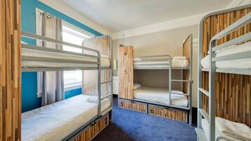 A bunk room with three bunk beds, each with a number label, and a window with curtains.