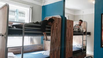 Ein Schlafsaalzimmer mit Etagenbetten, Holztrennwänden und einem Fenster mit Vorhängen.