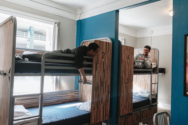 Un dormitorio con literas, separadores de madera y una ventana con cortinas.