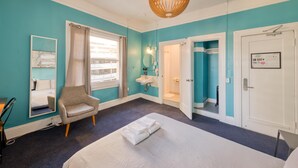 A hotel room with a bed, a chair, a window with curtains, a sink, and a door. - HI San Francisco Downtown Hostel (San Francisco)
