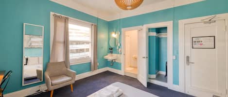 A hotel room with a bed, a chair, a window with curtains, a sink, and a door.