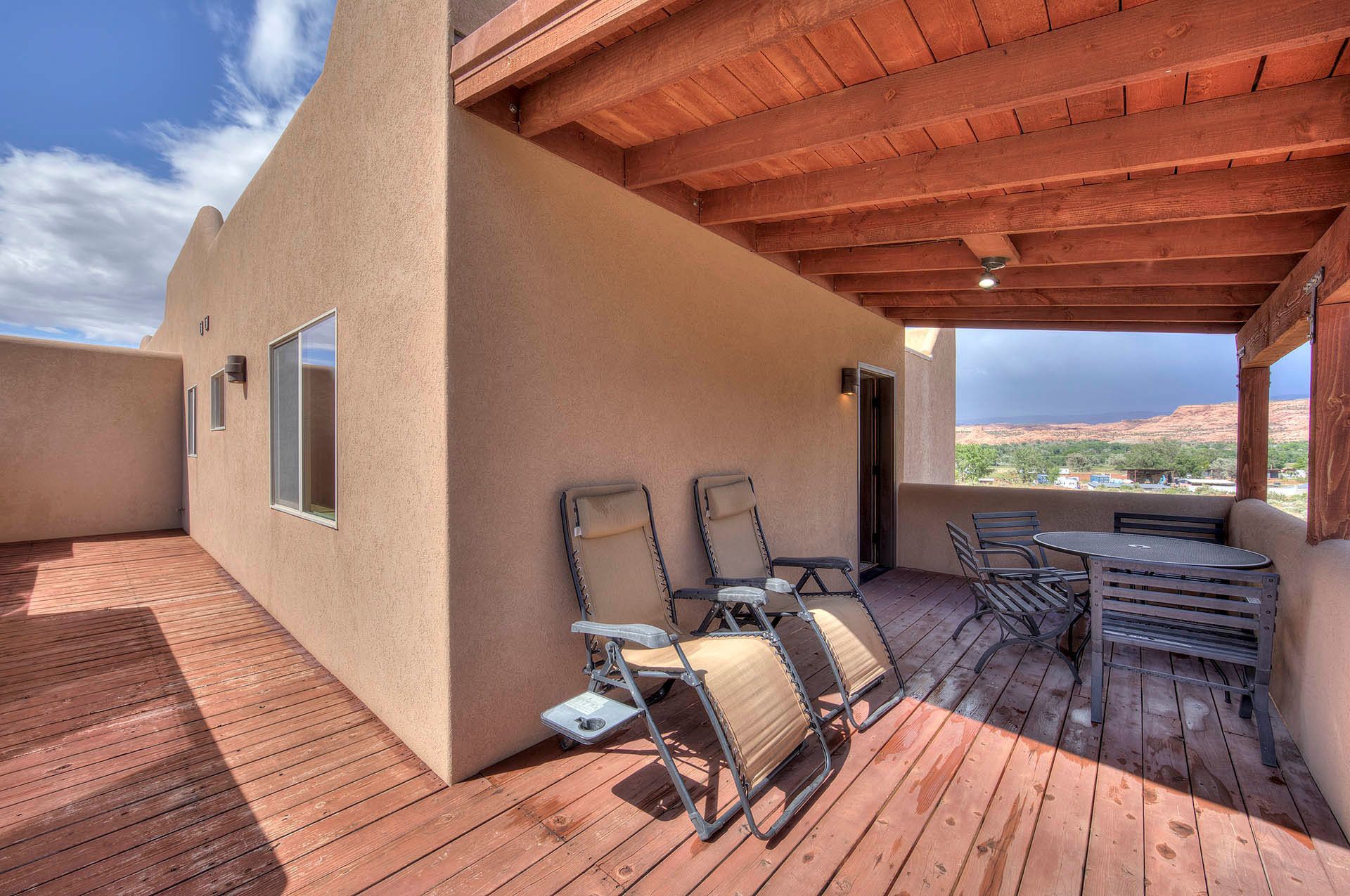 A covered patio with a wooden ceiling, a table with chairs, and a view of the desert landscape.