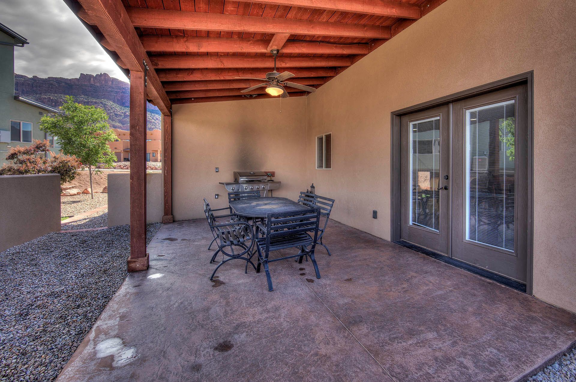 A covered patio with a table and chairs, a grill, and a sliding glass door.