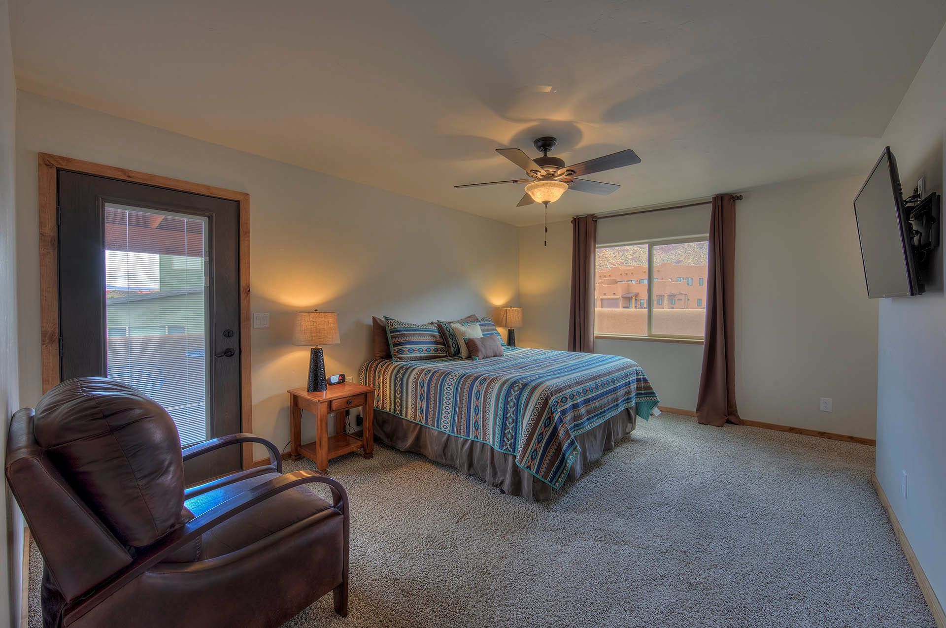 A bedroom with a bed, a chair, a ceiling fan, a window, and a door.