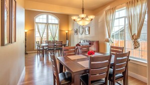 A dining room with a wooden table and chairs, a chandelier, and large windows with curtains. - Brookwood Manor (5 Bedroom, 14 Guests) (Hillsboro)
