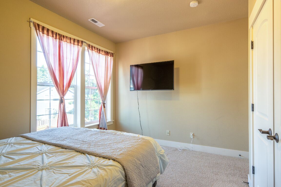 A bedroom with a bed, a TV mounted on the wall, and a window with curtains.