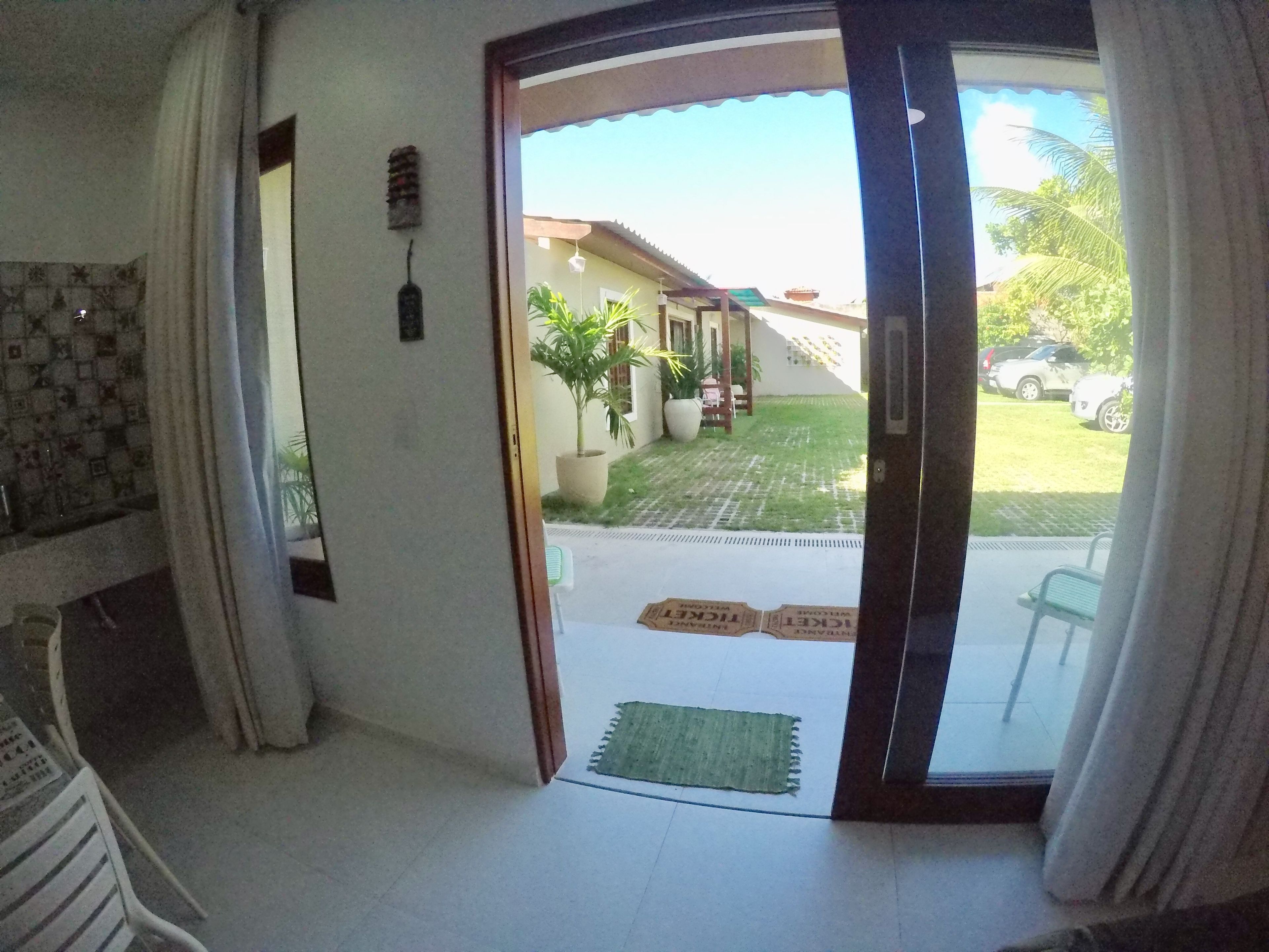 Una entrada con puerta de vidrio que da a un espacio exterior cubierto con césped, plantas en macetas y un coche estacionado.