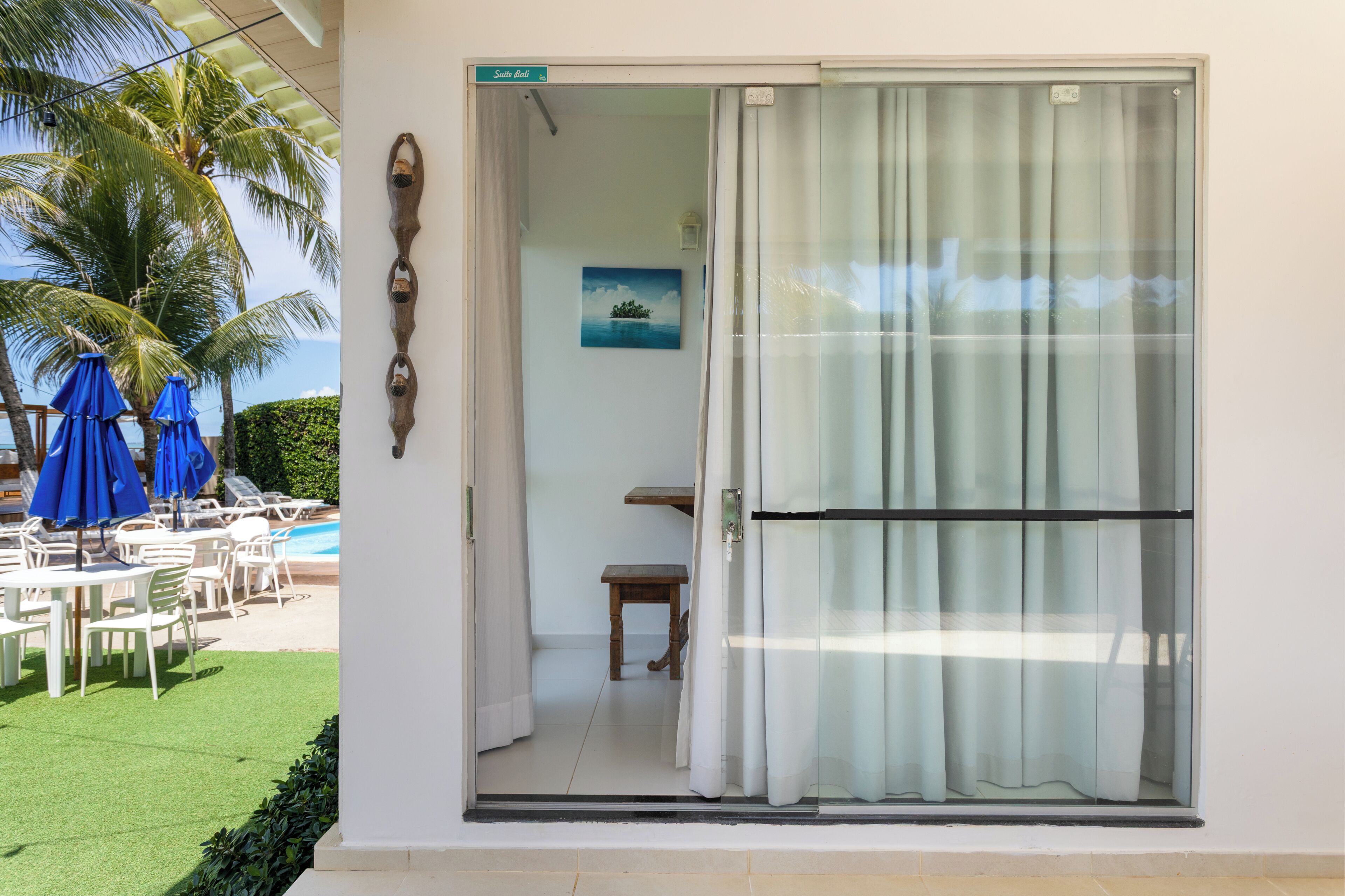 Quarto com porta de correr de vidro, uma mesinha, um banco e um quadro na parede.