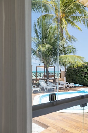 A pool area with lounge chairs, palm trees, and a view of the ocean. - Pousada Ipioca Beach Village (Maceió)