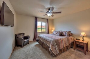 Ein Schlafzimmer mit Bett, Stuhl, Nachttisch, Lampe, Deckenventilator und einem Fenster mit Vorhängen.