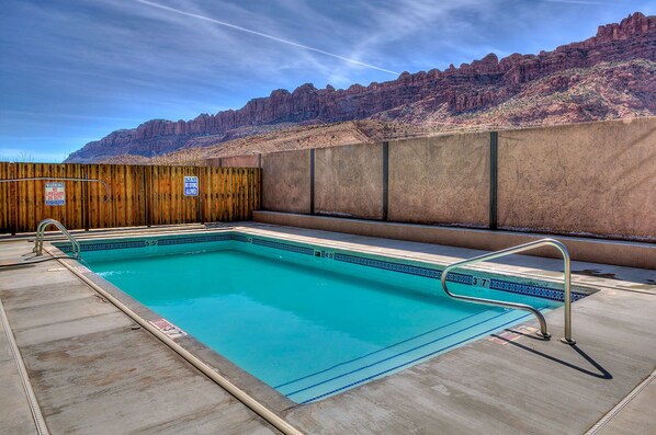 A swimming pool with a wooden fence and a lifeguard sign, surrounded by a mountainous landscape.