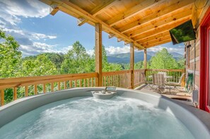 A hot tub with a control panel, surrounded by a wooden deck and a red door, overlooking a mountainous landscape. - Mount LeConte Views, Genuine Log Cabin, Hot Tub, Easy Access Near Town, Fire Pit (Gatlinburg)