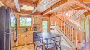 A wooden cabin interior with a kitchen, dining area, and a wooden staircase. - Mount LeConte Views, Genuine Log Cabin, Hot Tub, Easy Access Near Town, Fire Pit (Gatlinburg)