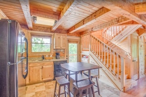 Cozy cabin interior with a fully equipped kitchen, featuring a refrigerator, coffee maker, and wooden cabinets. A staircase leads to an upper level.