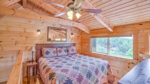 A wooden cabin bedroom with a bed, a ceiling fan, a window, and a small table. - Mount LeConte Views, Genuine Log Cabin, Hot Tub, Easy Access Near Town, Fire Pit (Gatlinburg)