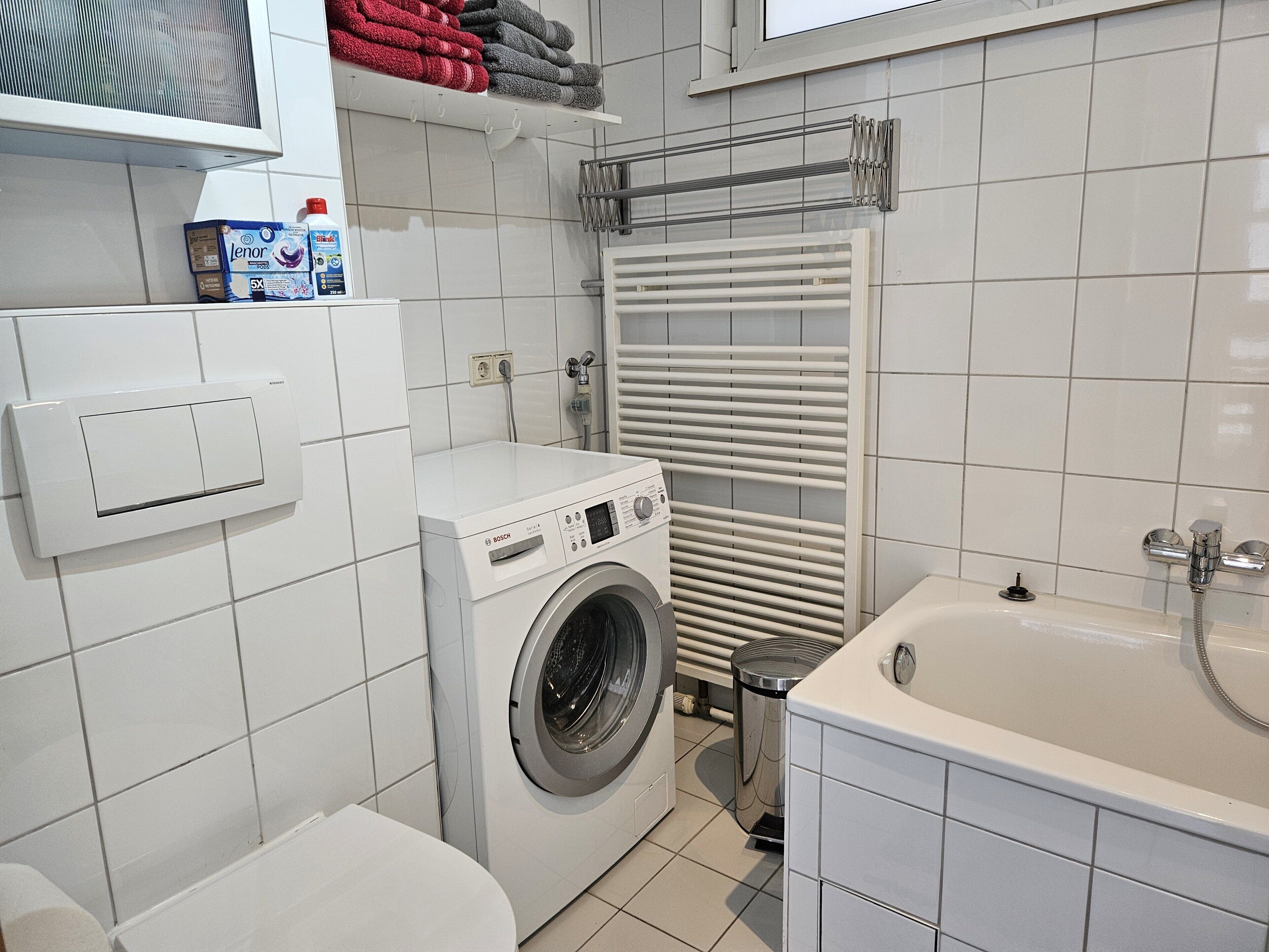 Une petite buanderie équipée d’un lave-linge, d’un sèche-linge, d’un porte-serviettes avec des serviettes pliées et d’un thermostat fixé au mur.