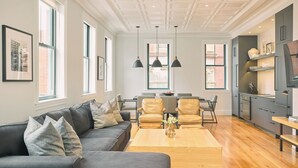 Ein modernes Wohnzimmer mit einer Couch, einem Couchtisch und Sesseln. Es gibt eine Küchenzeile mit Schränken und einem Kühlschrank.