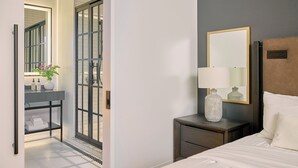 Ein Hotelzimmer mit Bett, Nachttisch mit Lampe, Spiegel und Badezimmer mit Waschbecken und Dusche.