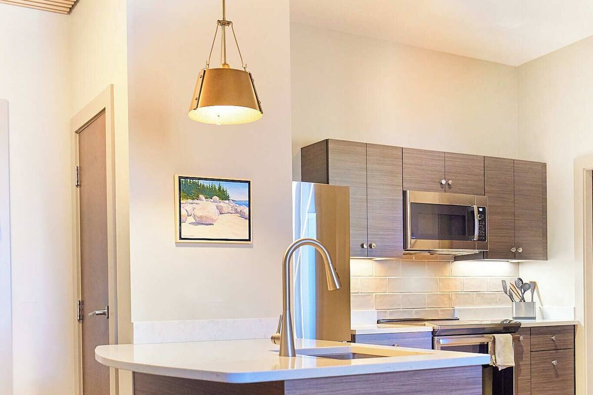 A modern kitchen with a central island, bar stools, a microwave, and a sink.