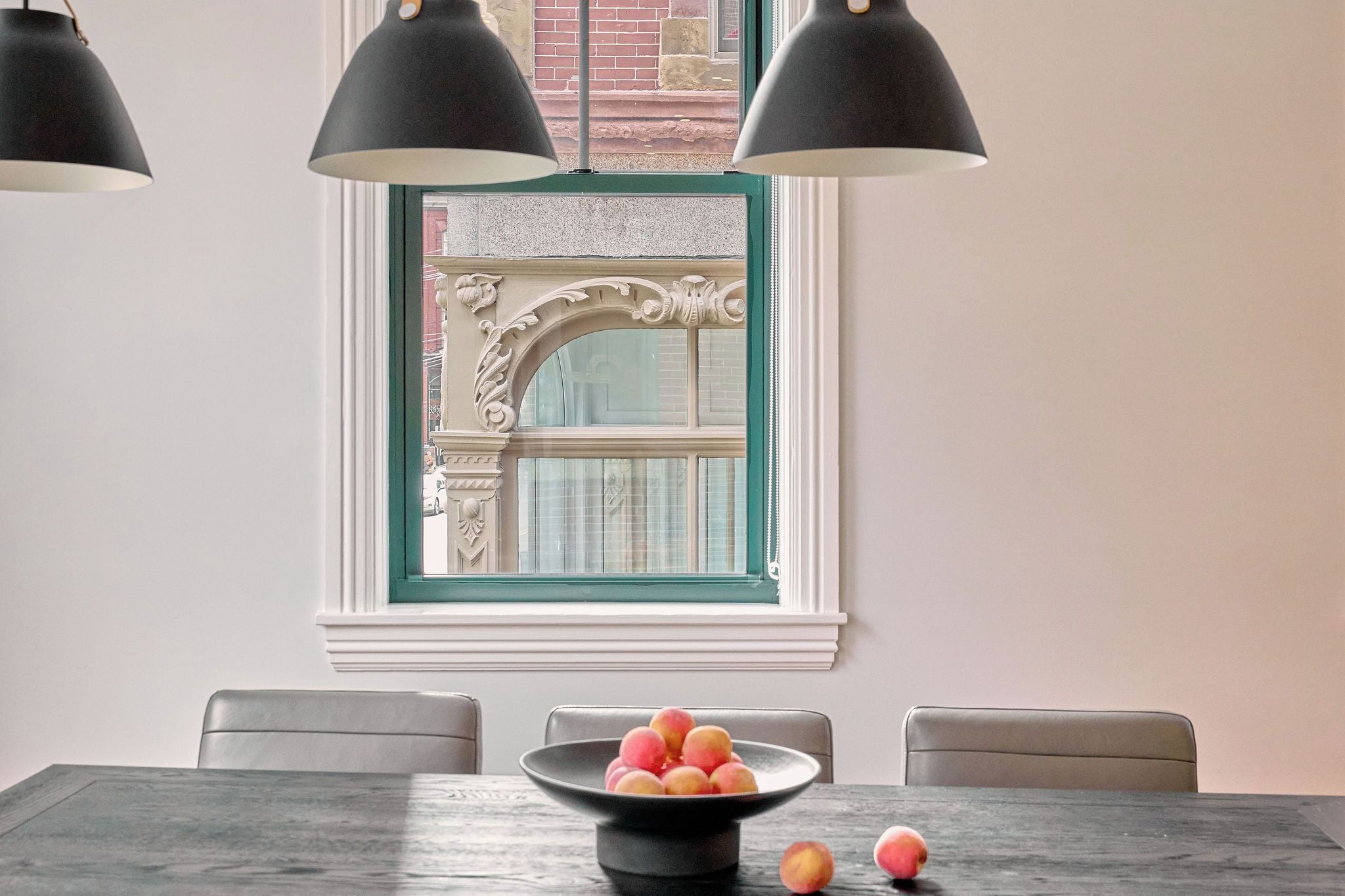 Un comedor con una mesa, sillas, un tazón de fruta y un ventanal decorativo con marco verde.