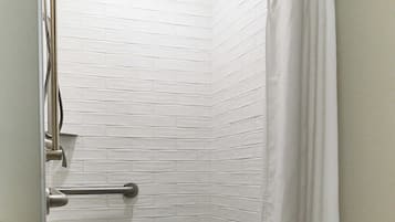 A shower with white tiled walls, a handheld showerhead, a grab bar, and a white curtain.