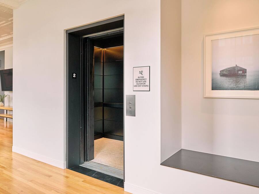 An elevator with a sign indicating emergency procedures, a framed picture on the wall, and a wooden floor.