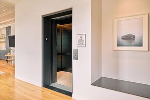 An elevator with a sign indicating emergency procedures, a framed picture on the wall, and a wooden floor.