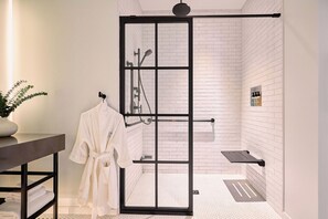 A modern bathroom with a glass shower enclosure, white tiled walls, a black metal shower rod, and a towel rack with a white bathrobe.
