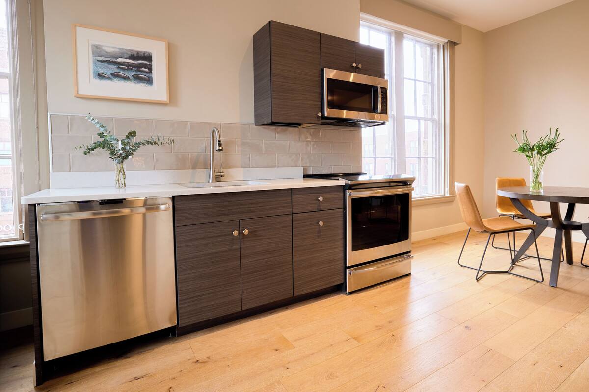 A modern kitchen with a dishwasher, oven, microwave, and a dining area with a table and chairs.