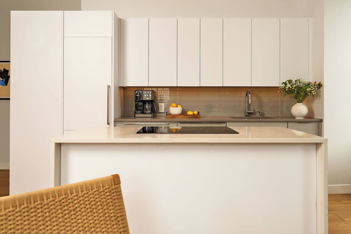 A modern kitchen with white cabinetry, a built-in oven, a coffee maker, and a small plant on the counter.