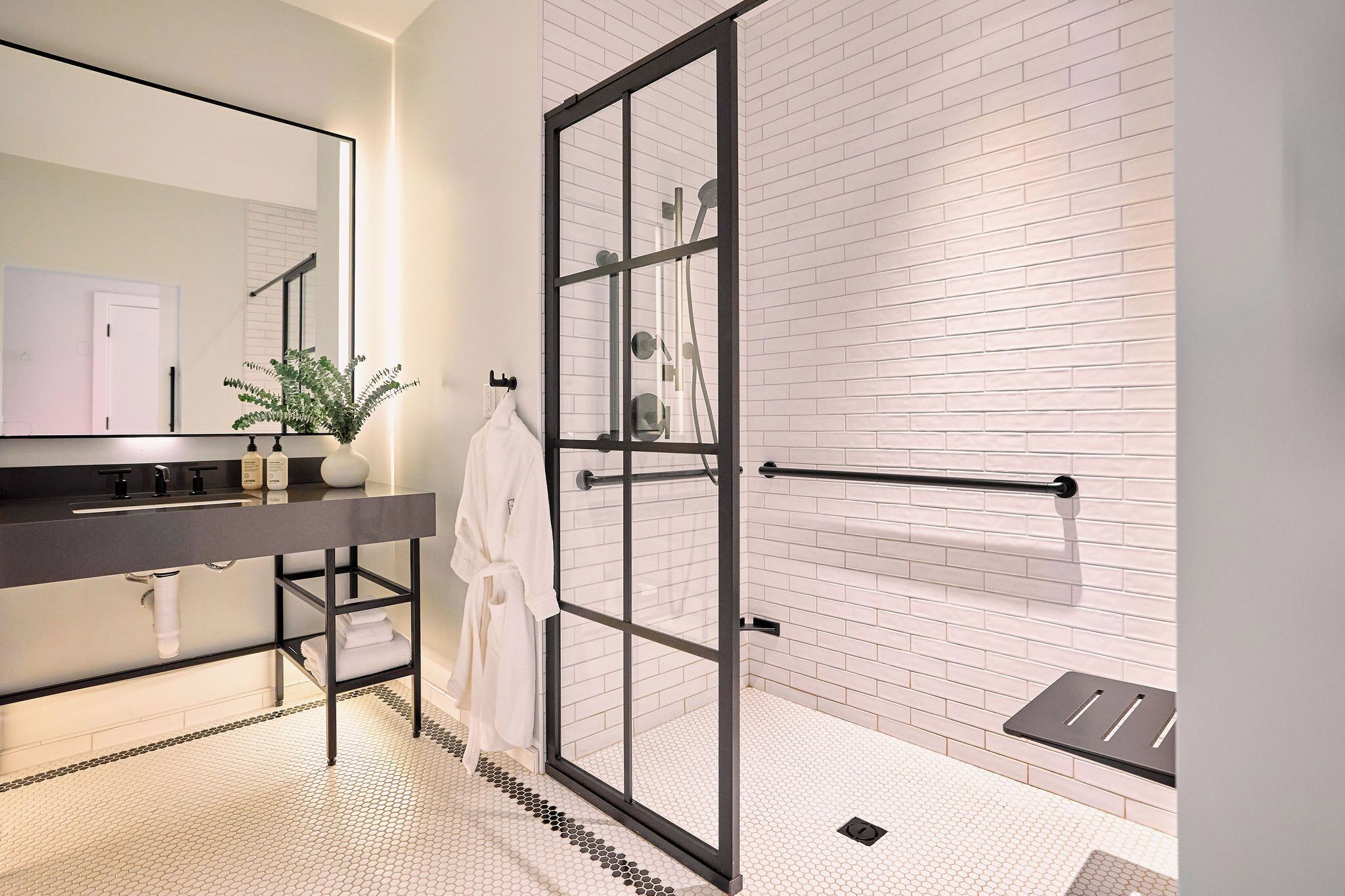 A modern bathroom with a large mirror, a black sink, a glass-enclosed shower, and a white tiled floor.