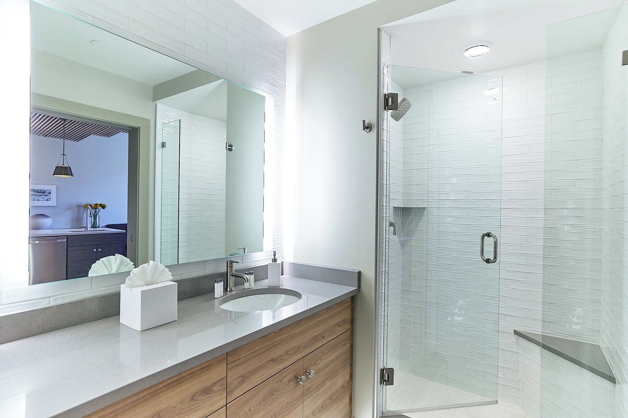 Ein modernes Badezimmer mit Duschkabine aus Glas, einem großen Spiegel und einem Holzlagerfläschchen.