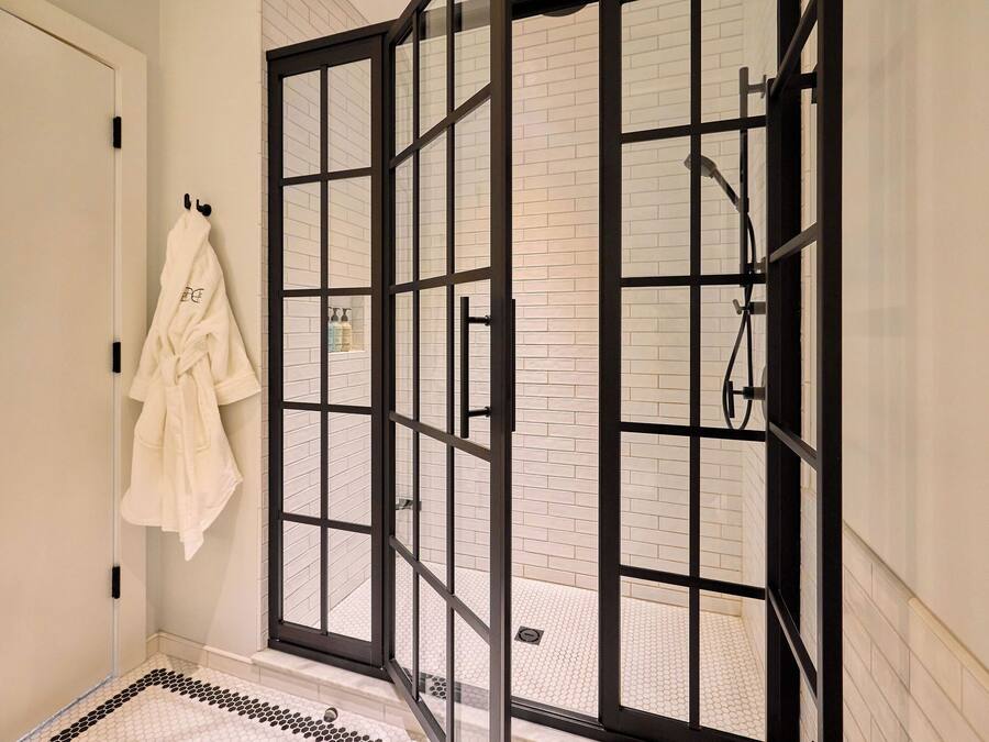 A shower with a glass door, a towel hanging on the wall, and a tiled floor.